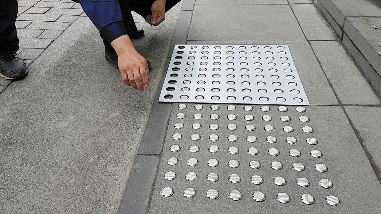 Installer fitting a stainless steel tactile tile with studs on a concrete pavement